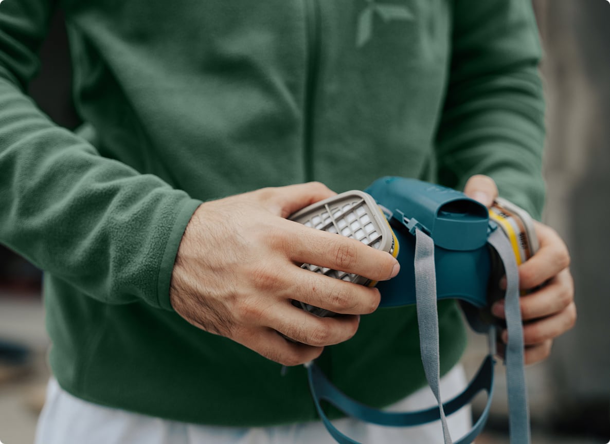 Dettaglio delle mani di un tecnico mentre svita i filtri di una maschera respiratoria.